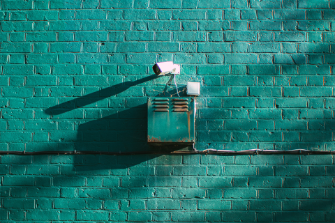 A surveillance camera on a green bricked wall 